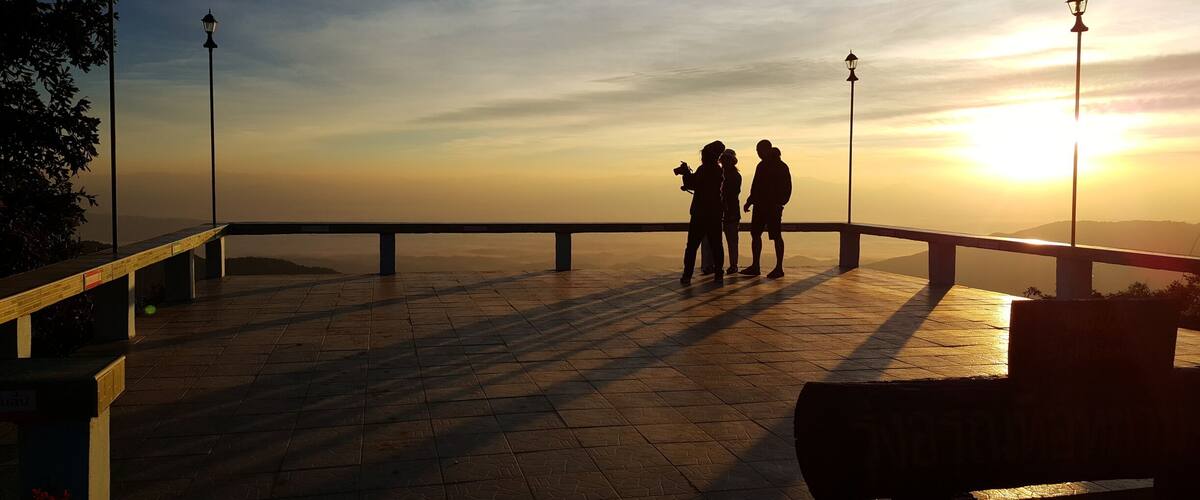 A sunset over a paved viewing platform with railings and street lamps.