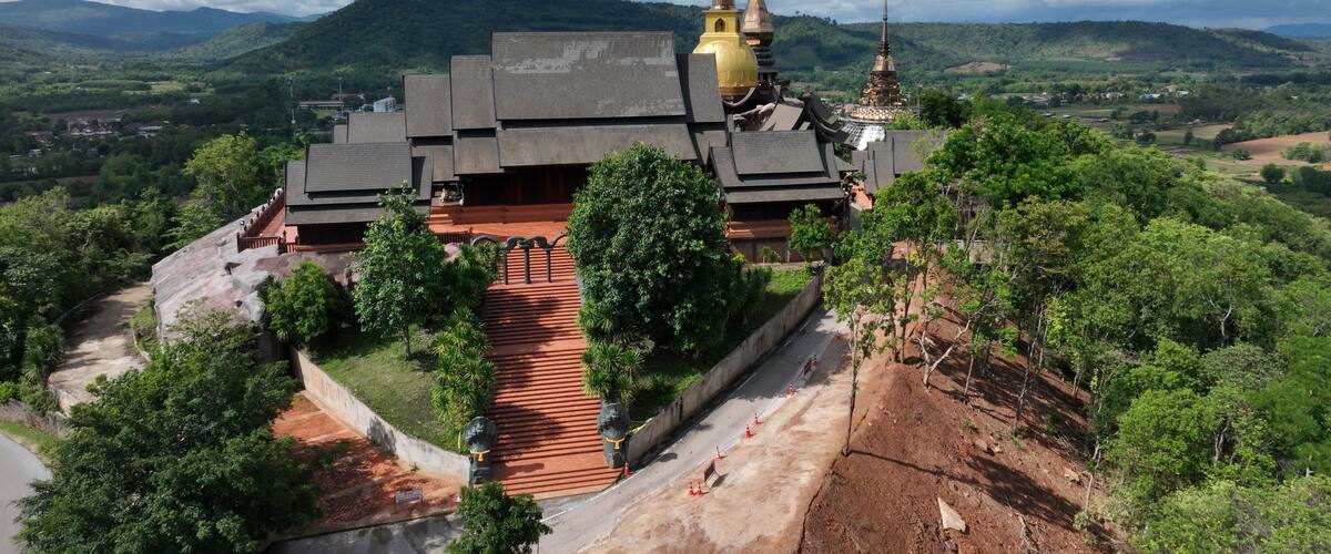 A temple complex with multiple spires, surrounded by lush greenery and hills in the background.