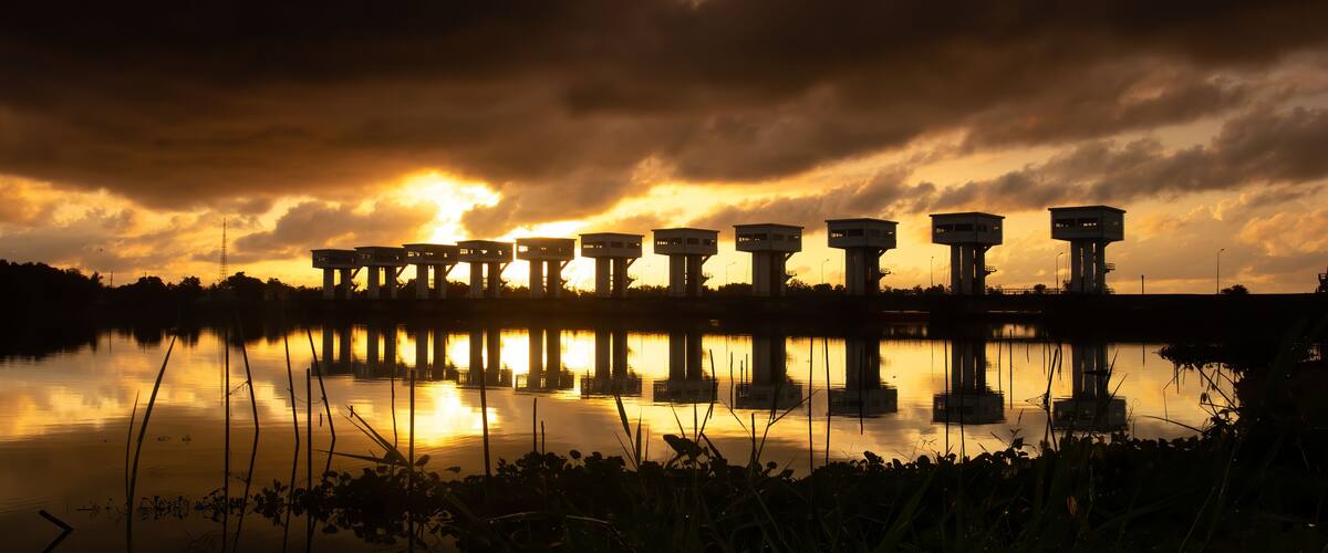 A sunset over a body of water with several structures reflected in the water.