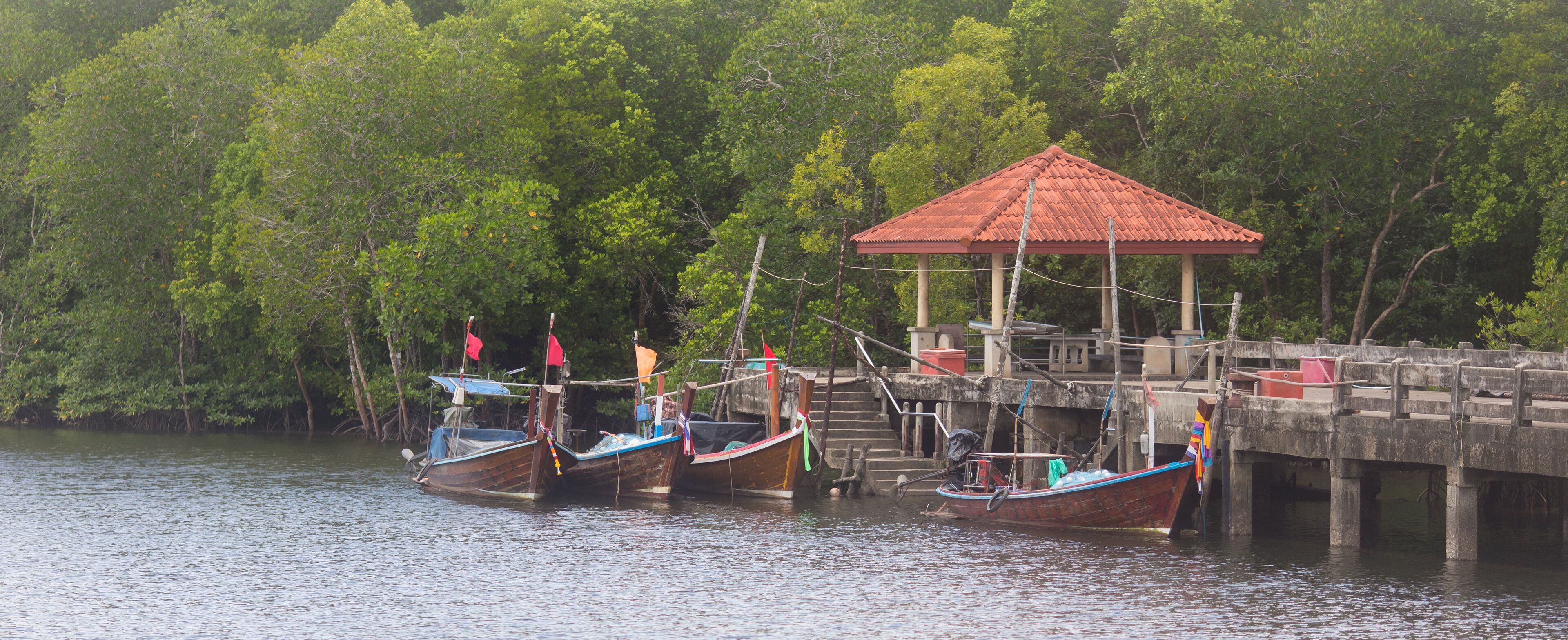 Three traditional boats docked at a pier with a red-roofed shelter.