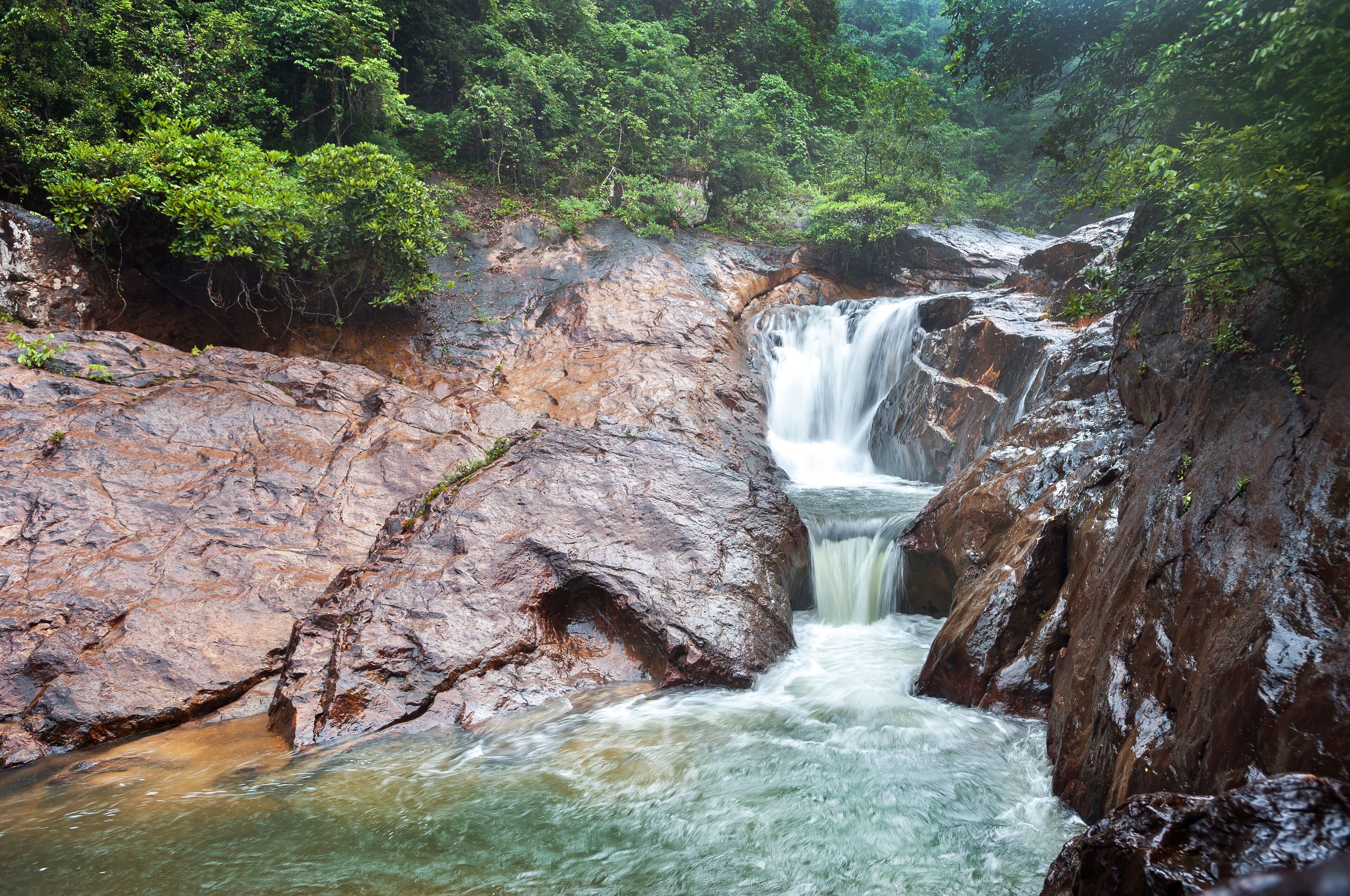 A waterfall cascading over rocky terrain surrounded by dense green foliage.