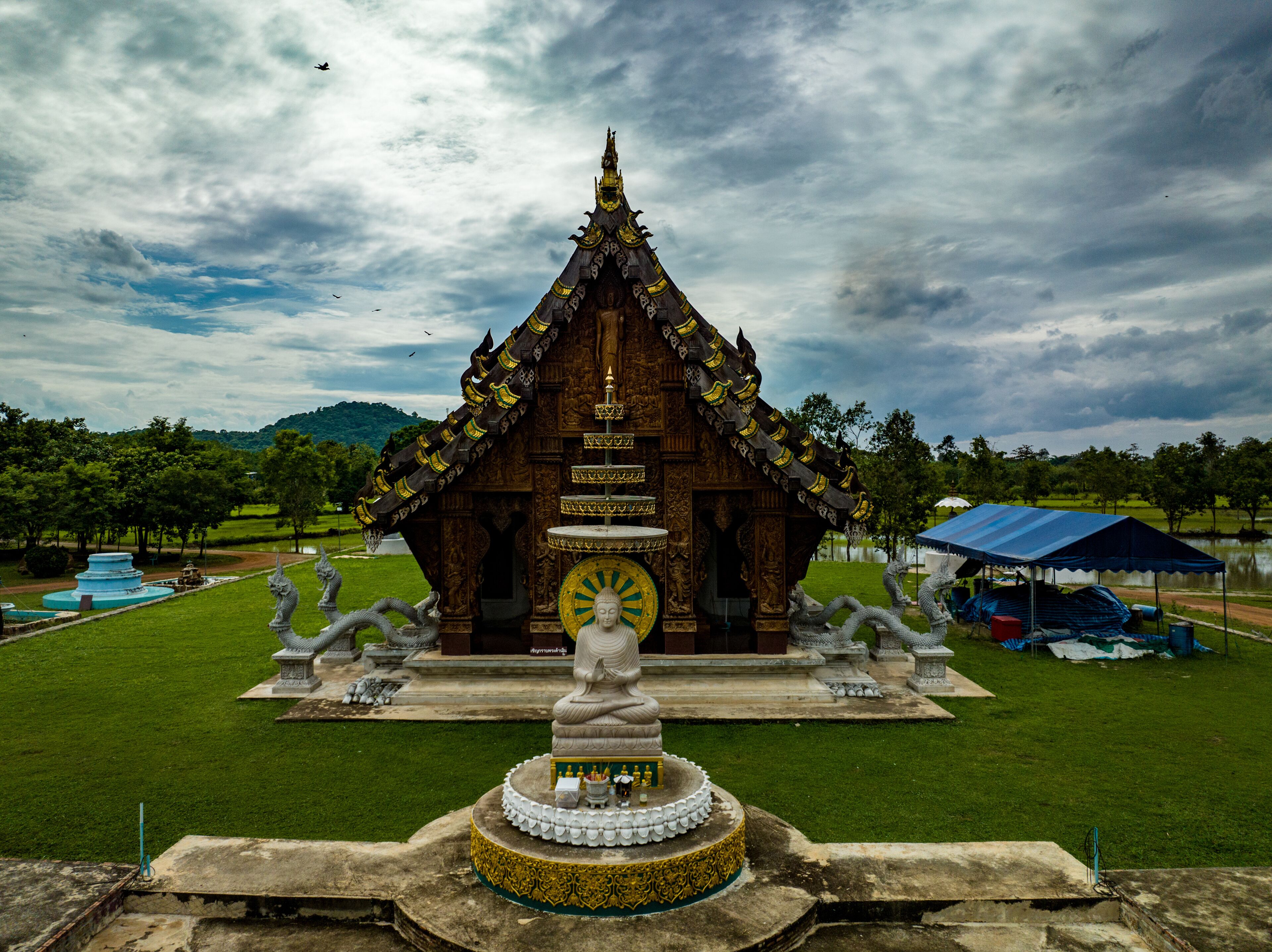 Chachoengsao, Thailand, 28 July 2023. Wat Nong Rua, Wooden temple with a red roof and intricate carvings. In front of the temple is a large statue of a seated Buddha.