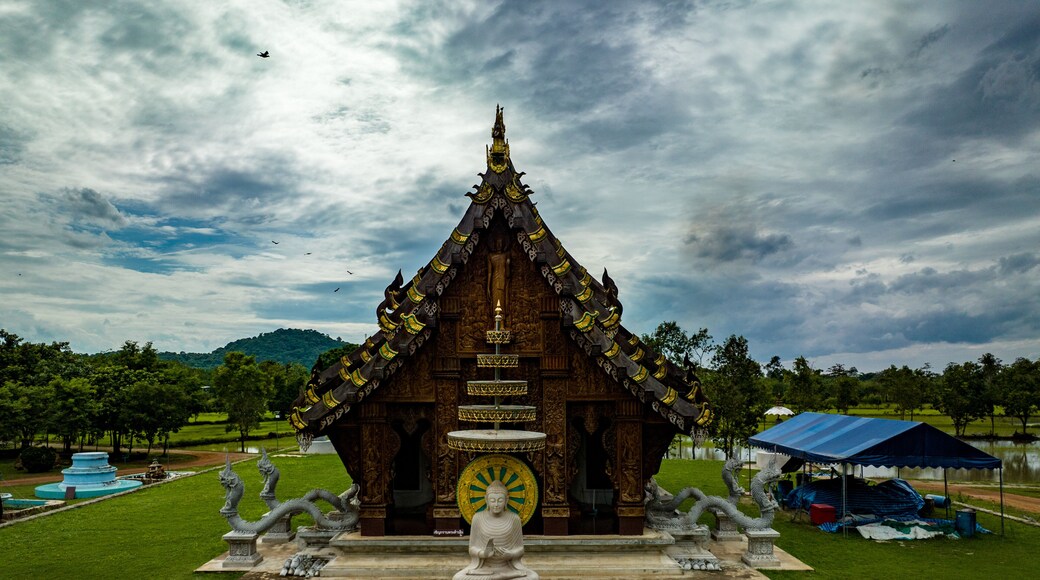 Chachoengsao, Thailand, 28 July 2023. Wat Nong Rua, Wooden temple with a red roof and intricate carvings. In front of the temple is a large statue of a seated Buddha.