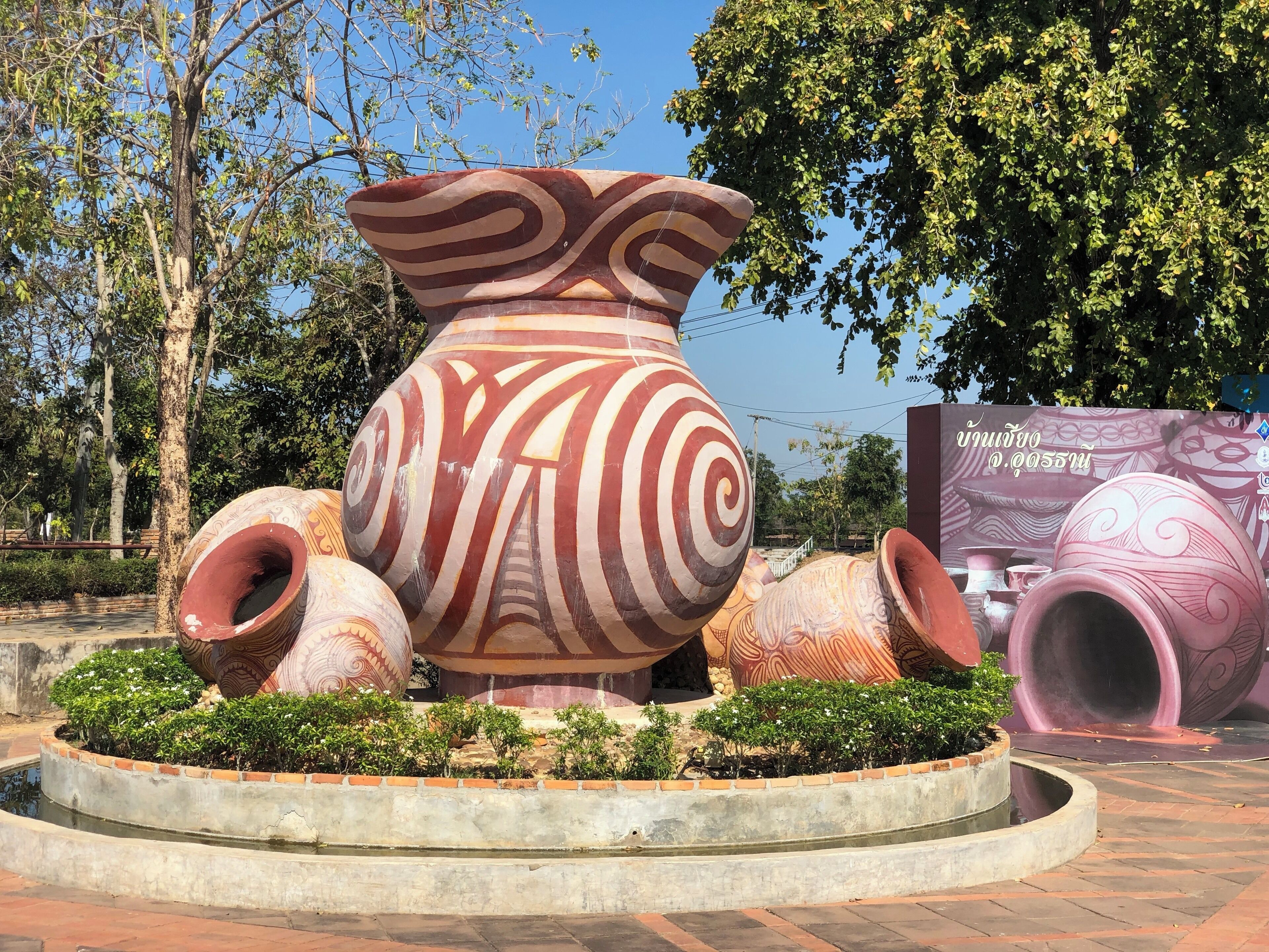 A large decorative pottery installation with intricate patterns, surrounded by a circular water feature and greenery.
