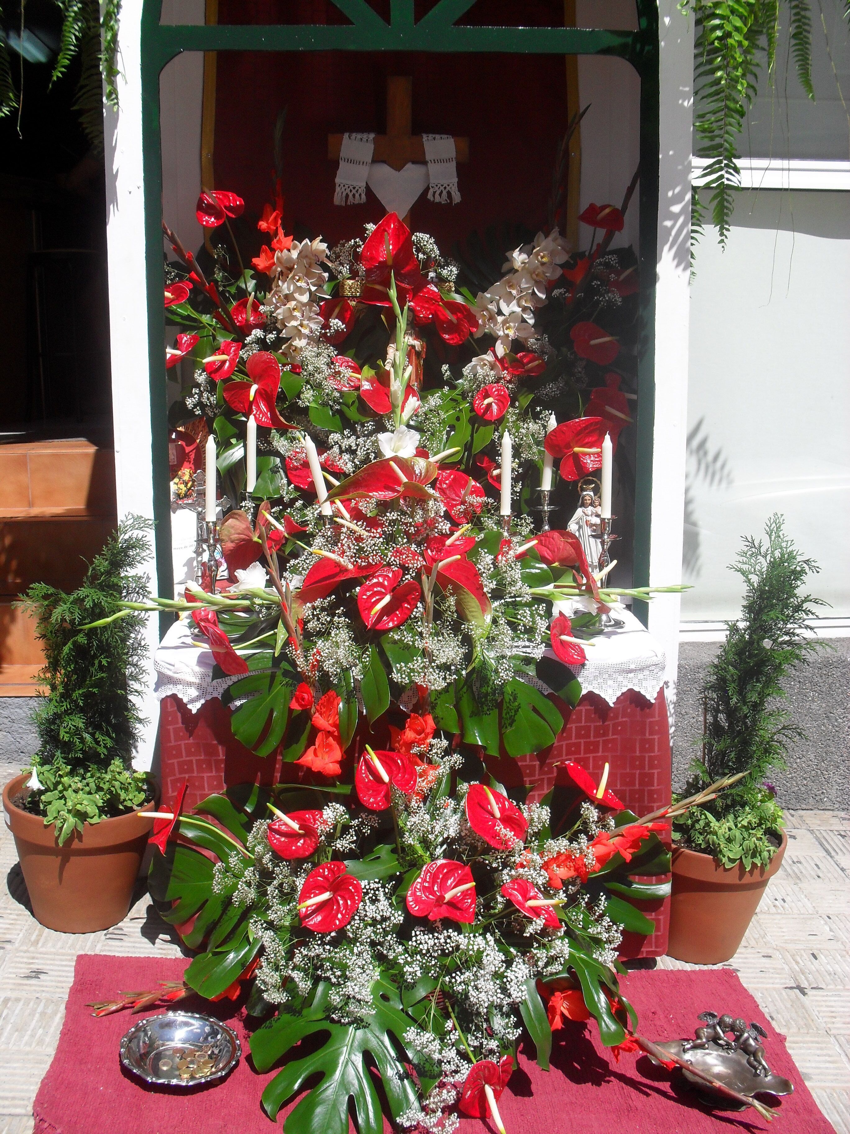 A shrine with red flowers, white candles, and a small statue.
