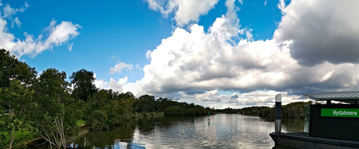 Een rivier met een steiger, bomen en een bewolkte lucht.