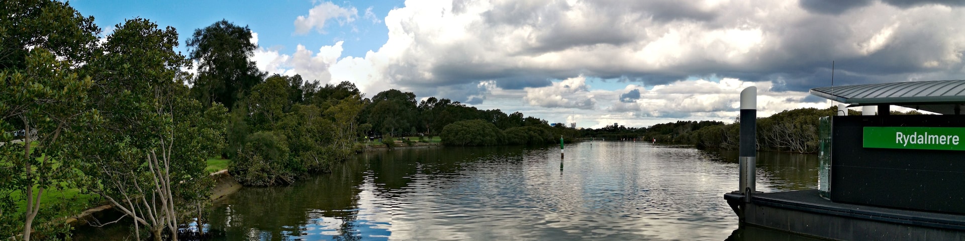 Un río con un muelle para barcos, árboles y un cielo nublado.