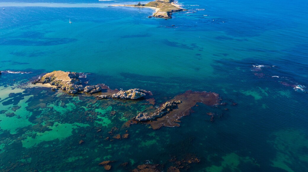 An aerial view of a coastal area with clear blue waters, rocky outcrops, and a sandy beach.