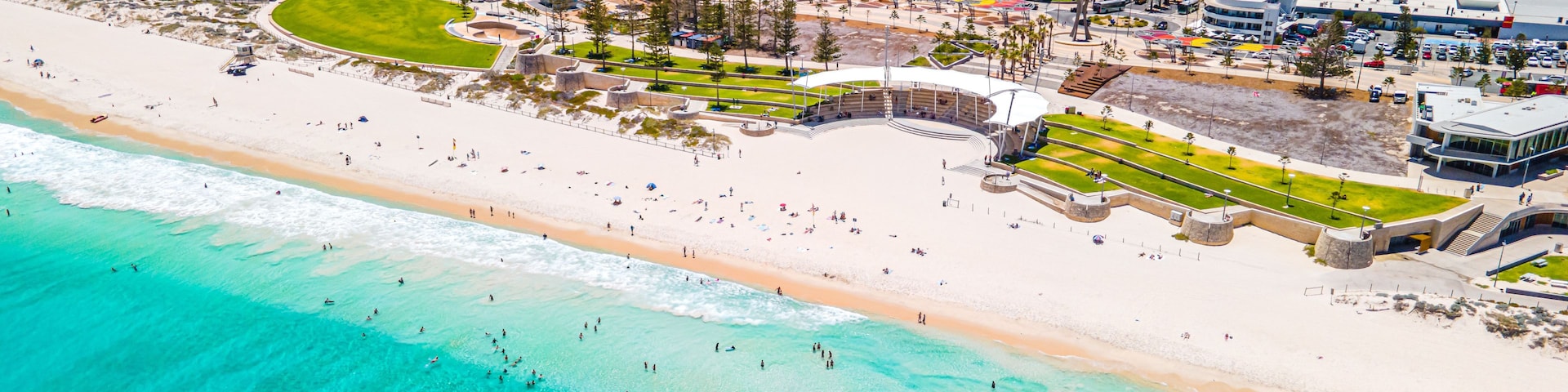 Un paisaje costero con playa arenosa, aguas turquesas cristalinas y edificios modernos.