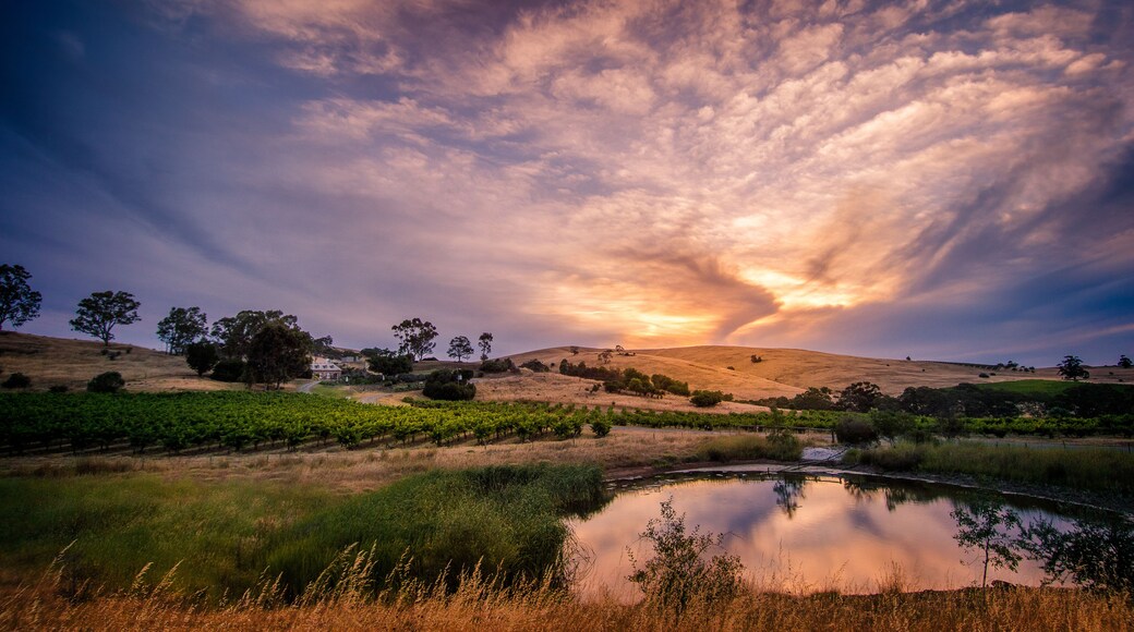 A sunset over a hilly landscape with a body of water reflecting the sky.