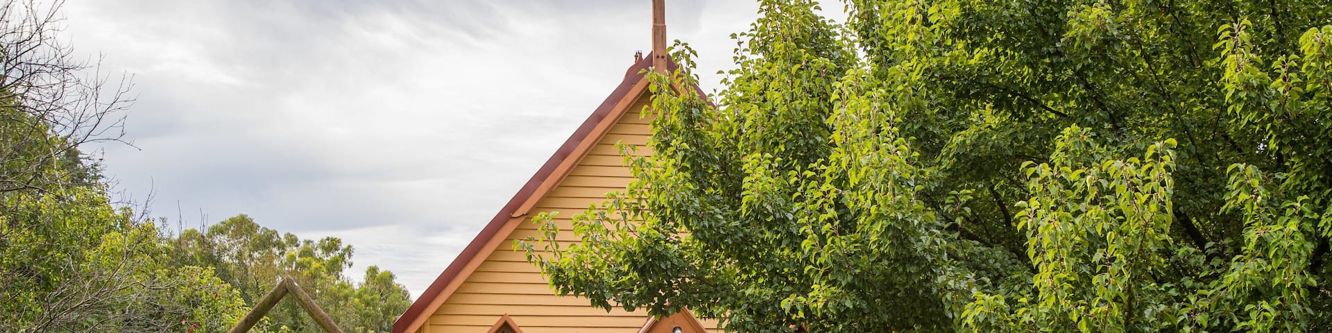 A small wooden church with a cross on top, surrounded by lush greenery and a bell tower.