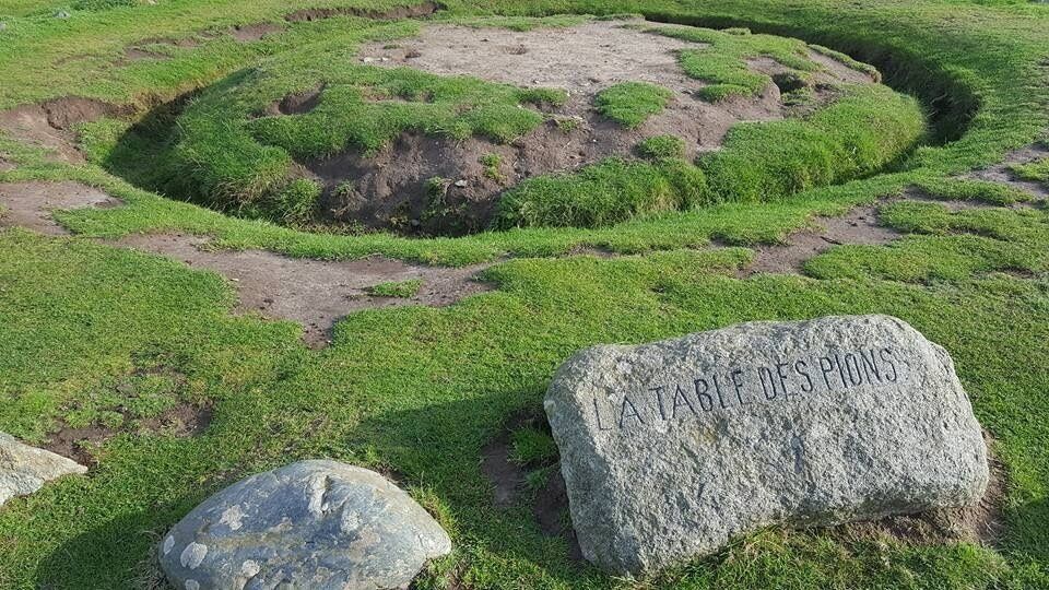 A circular stone structure with grass in the center and a large rock with inscriptions.