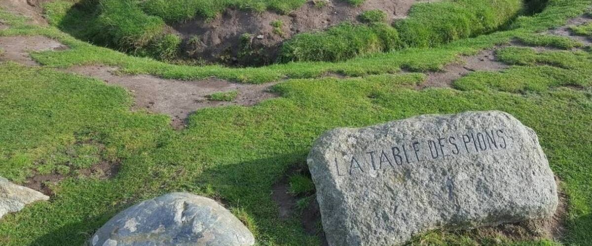 A circular stone structure with grass in the center and a large rock with inscriptions.