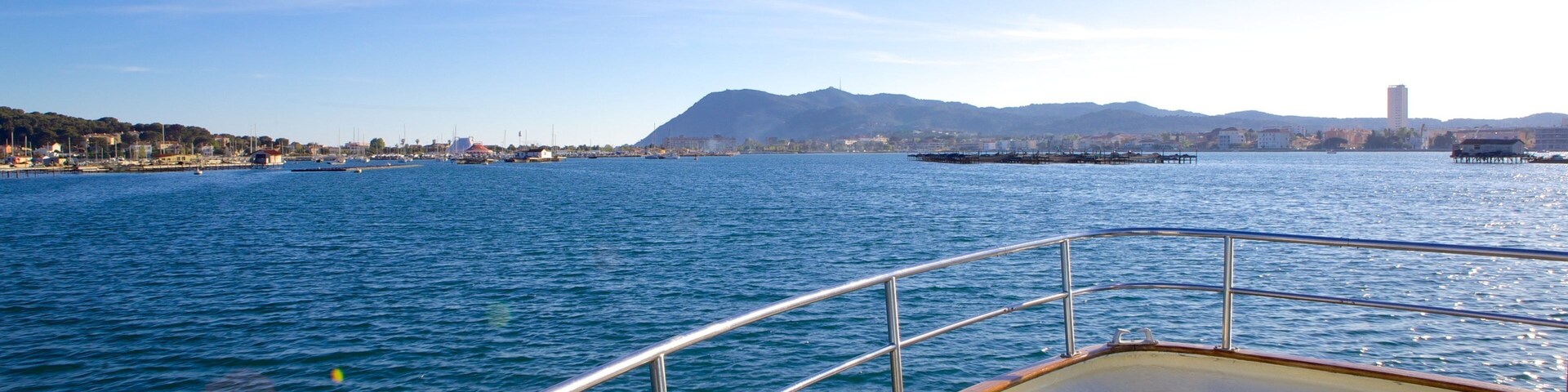 Un barco sobre un mar tranquilo con un paisaje urbano y montañas al fondo.