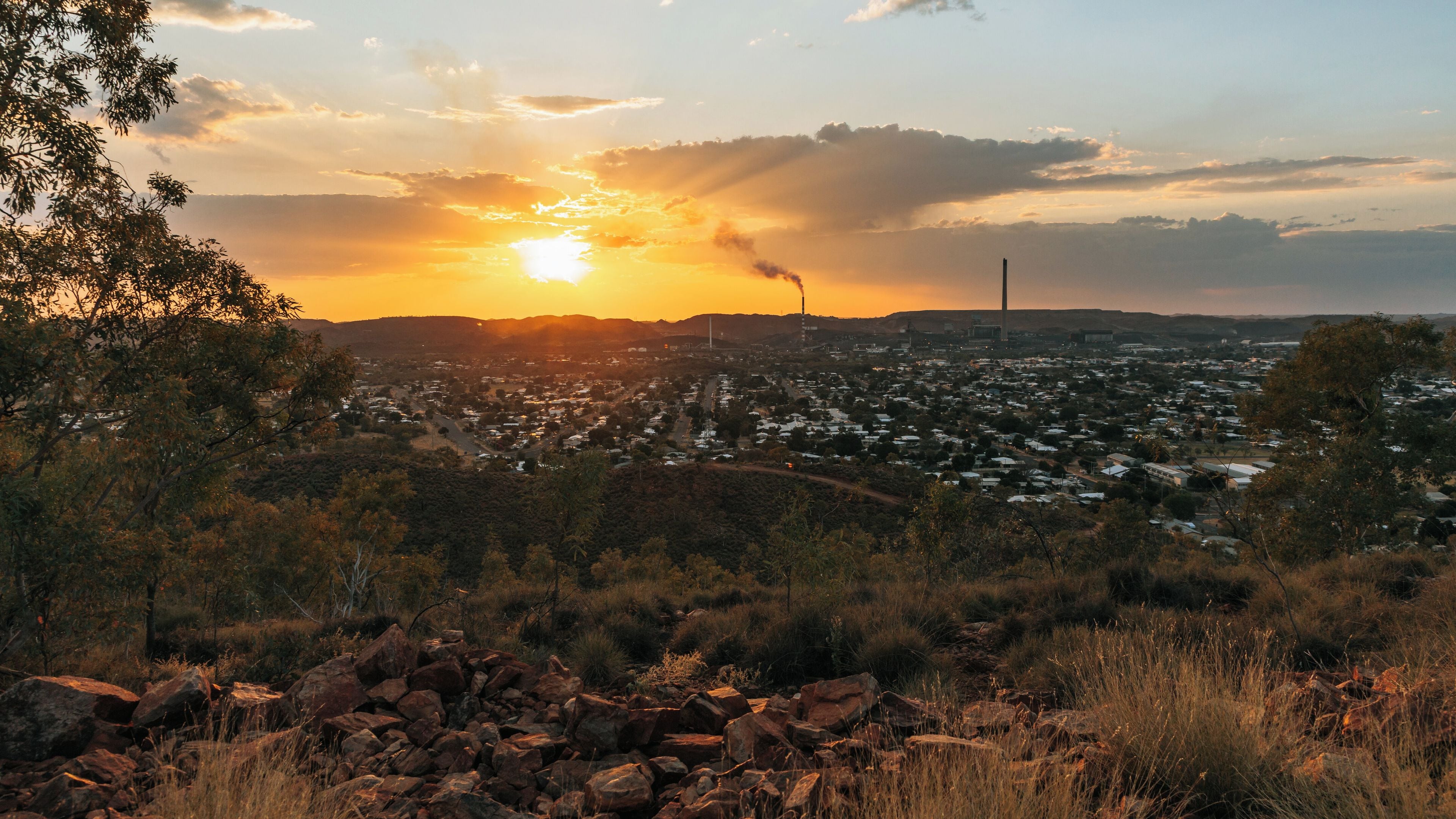A sunset over a city with a prominent smokestack and a dense residential area.