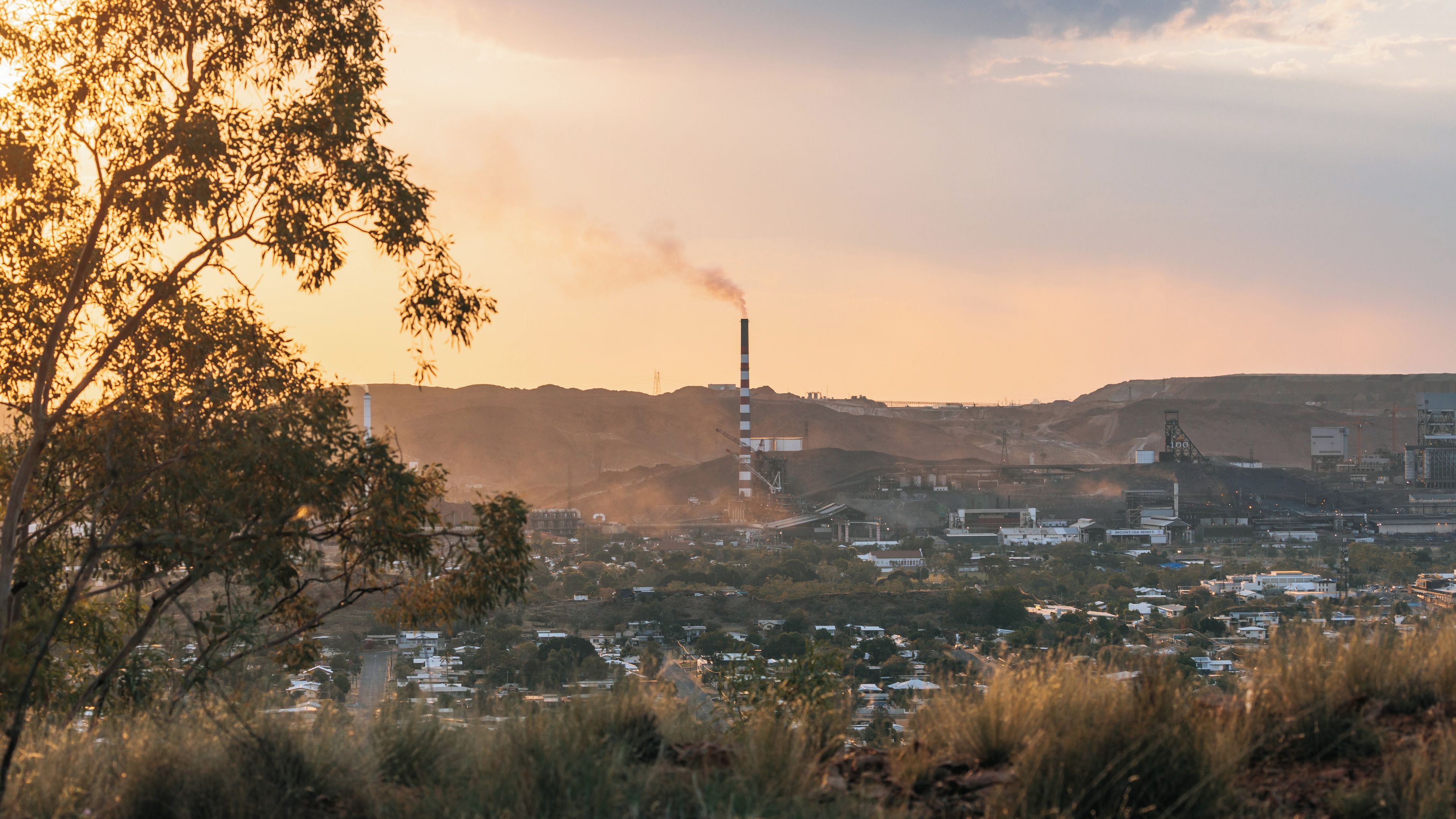 A landscape with a large industrial facility, a smokestack, and a residential area in the foreground.