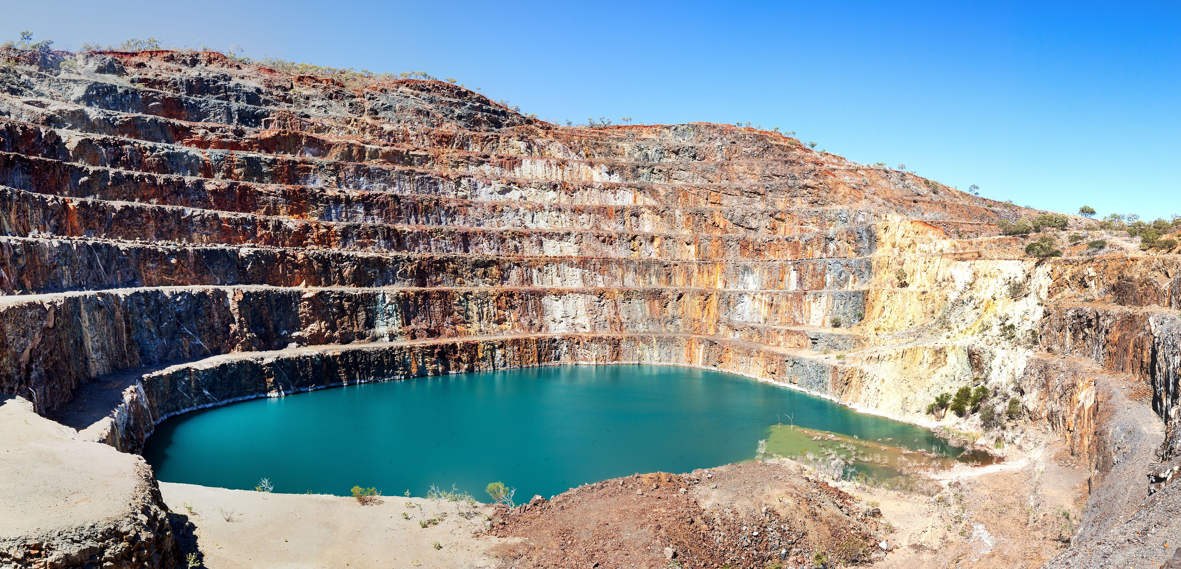 A large open-pit mine with a turquoise pool of water at its base.