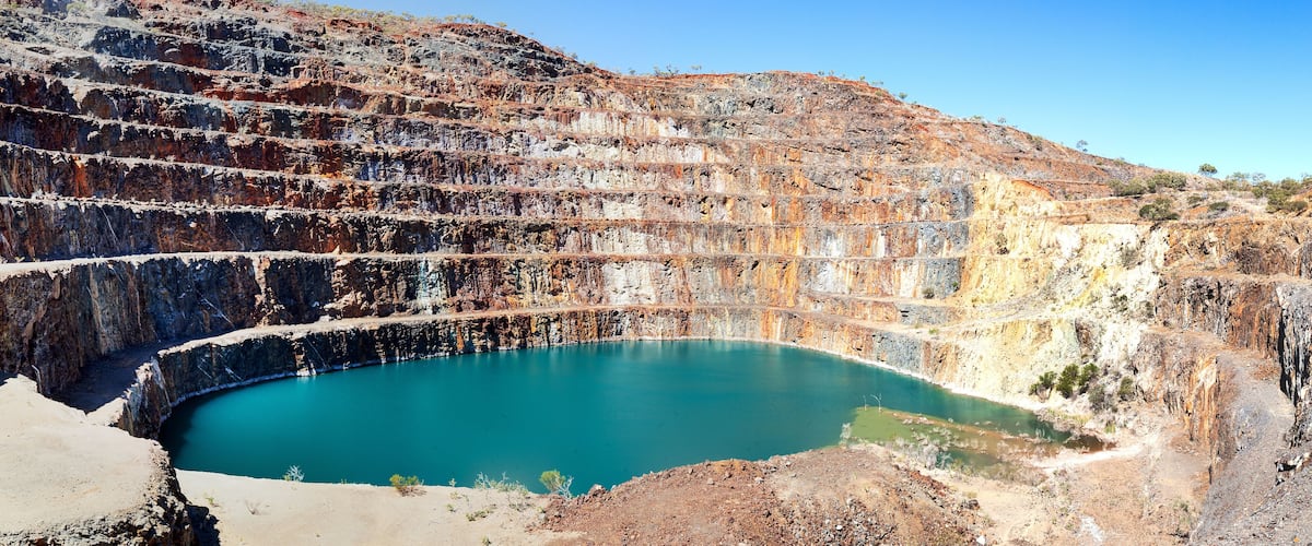 A large open-pit mine with a turquoise pool of water at its base.
