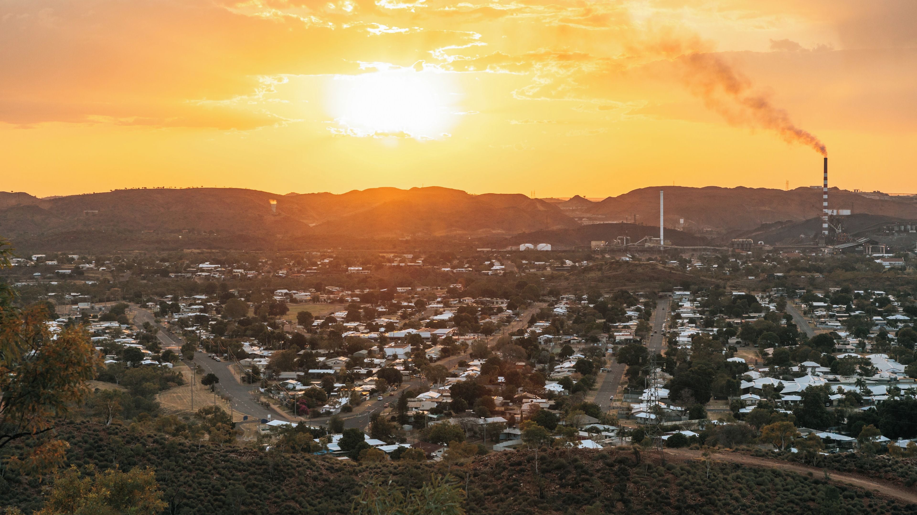 A sunset over a town with industrial buildings and smoke stacks.
