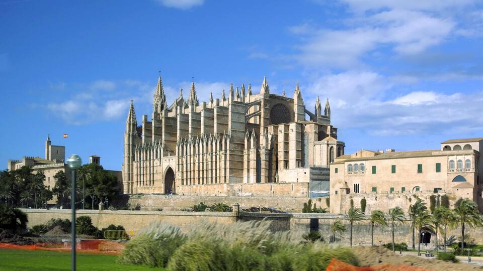 Une cathédrale historique à l’architecture gothique, dotée d’une grande rosace et entourée d’un paysage urbain où se côtoient palmiers et bâtiments modernes.