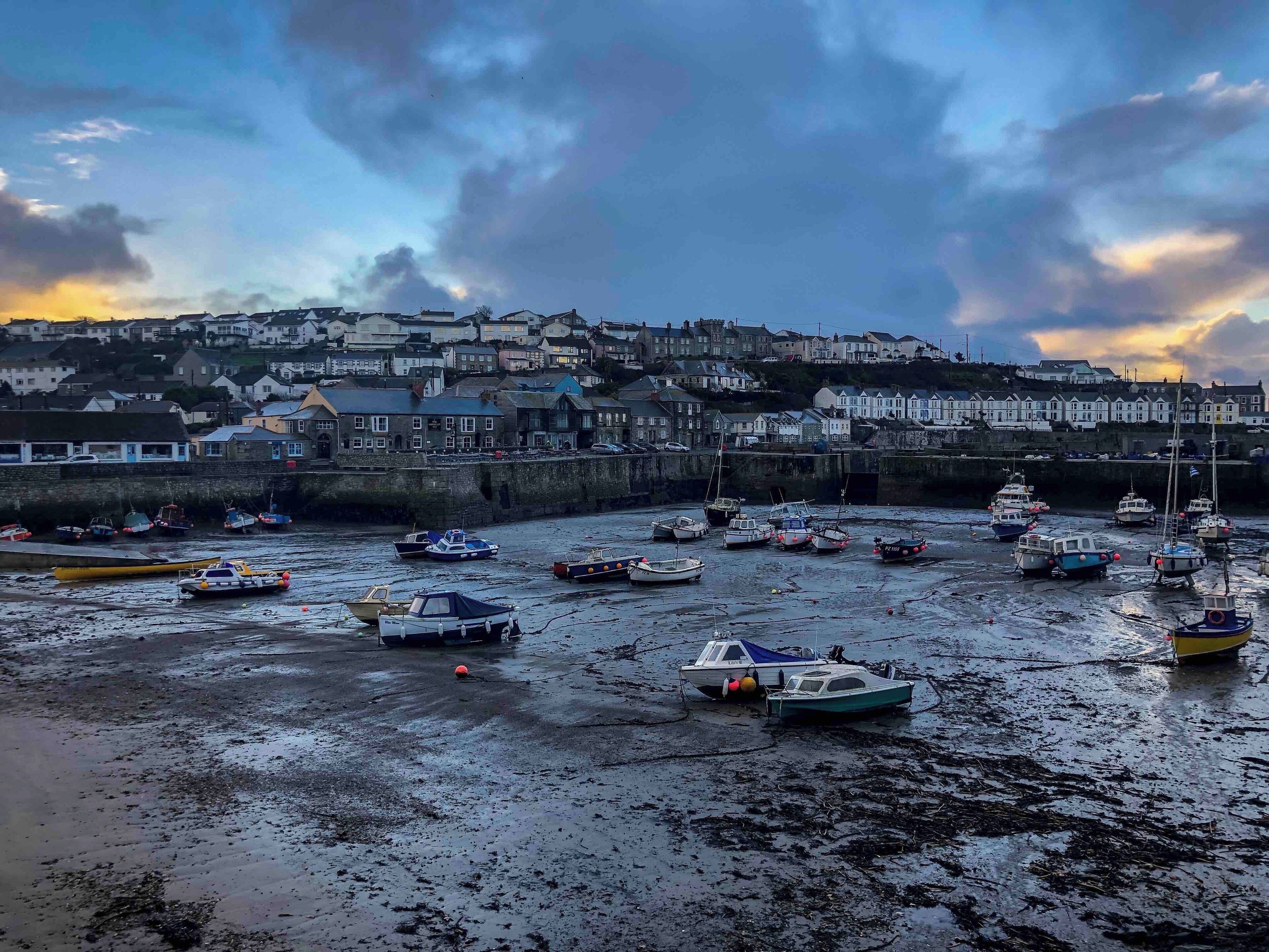 A coastal town with boats docked at low tide, houses in the background, and a cloudy sky.