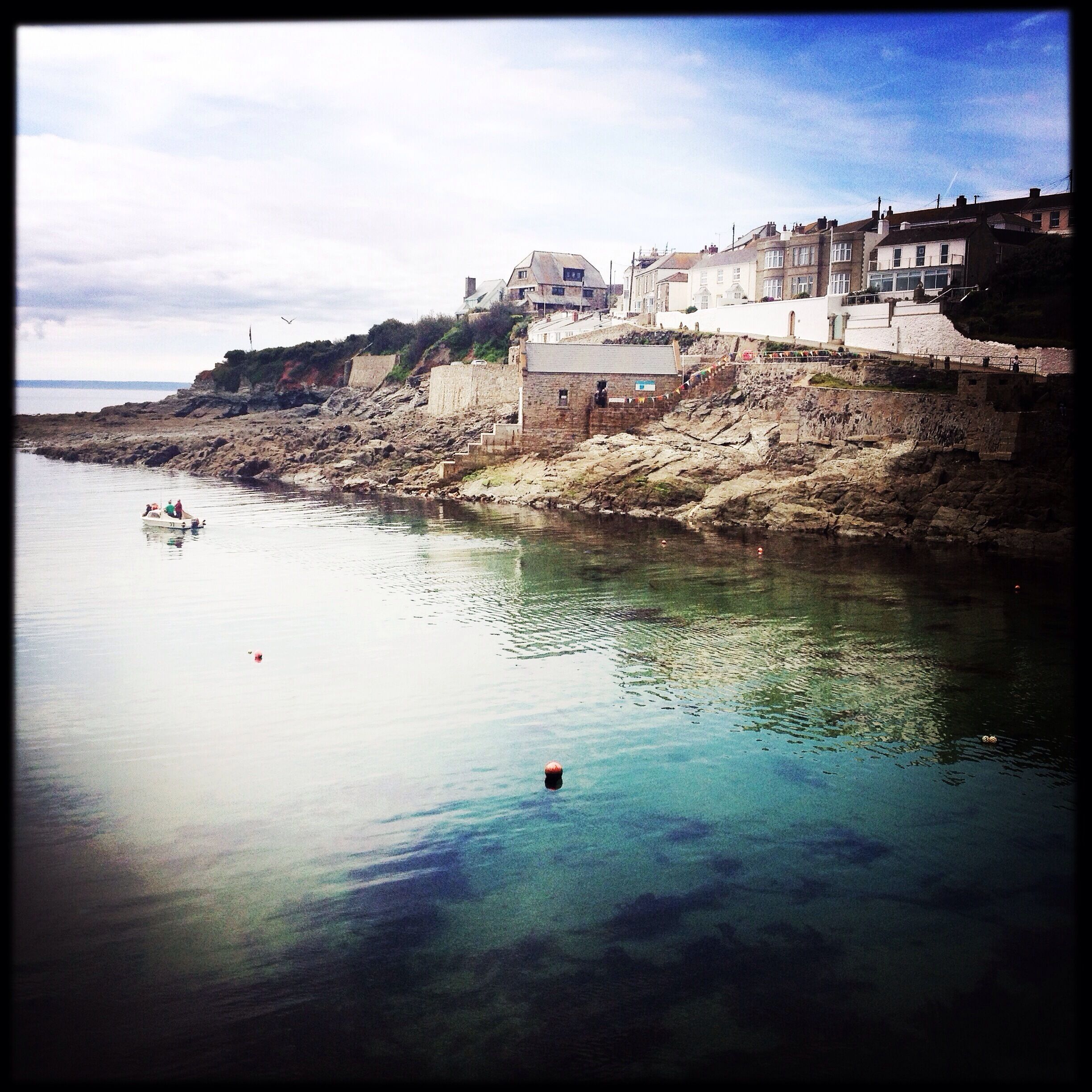 A coastal town with buildings on a cliff overlooking the sea, a boat on the water, and a buoy.