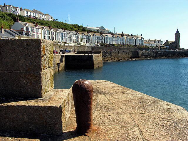A coastal town with stone piers, a lighthouse, and terraced houses along the water.