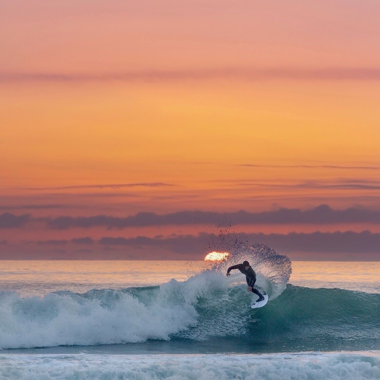 A surfer riding a wave at sunset.