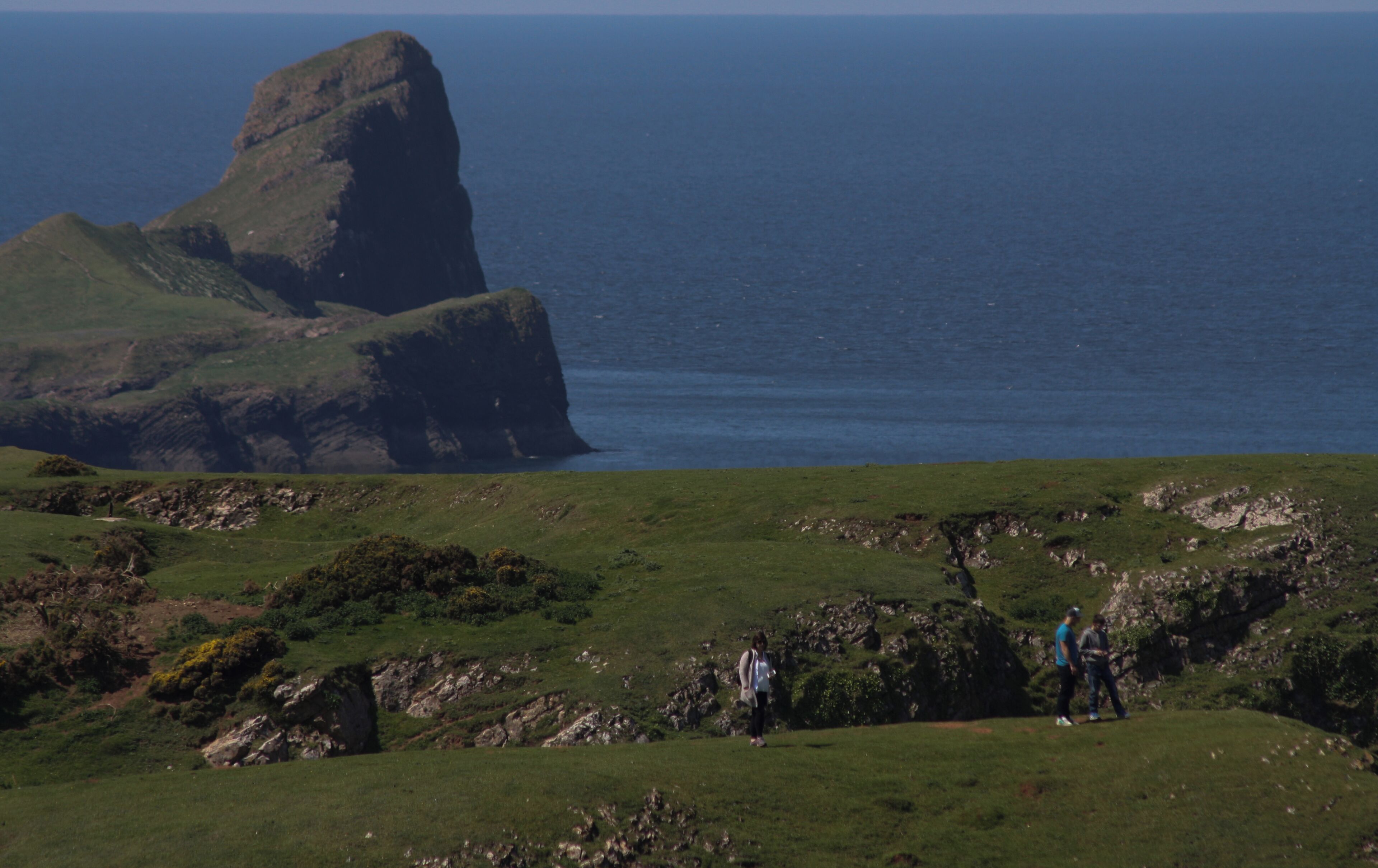 A grassy hill with a large rock formation and the ocean in the background.