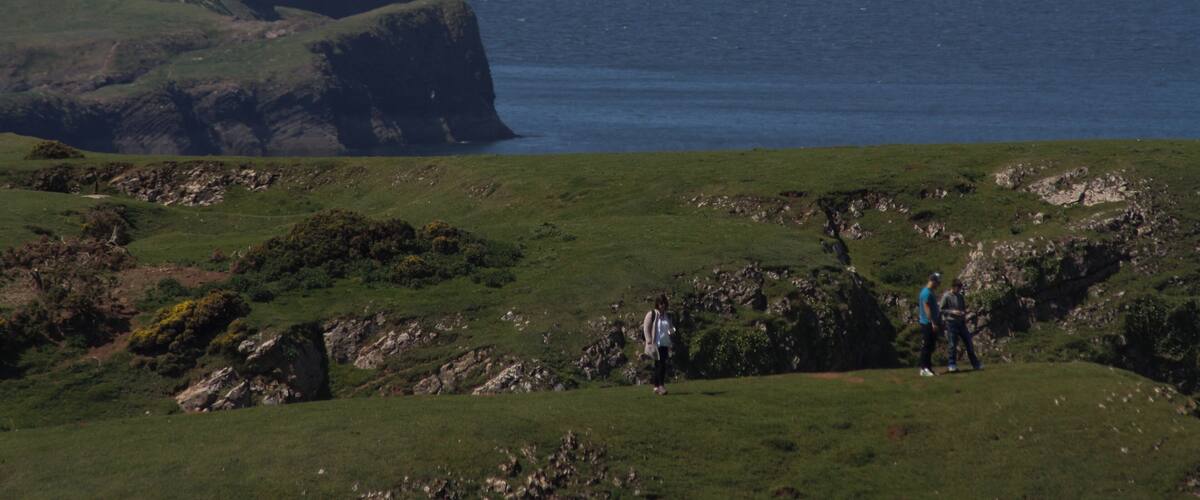 A grassy hill with a large rock formation and the ocean in the background.