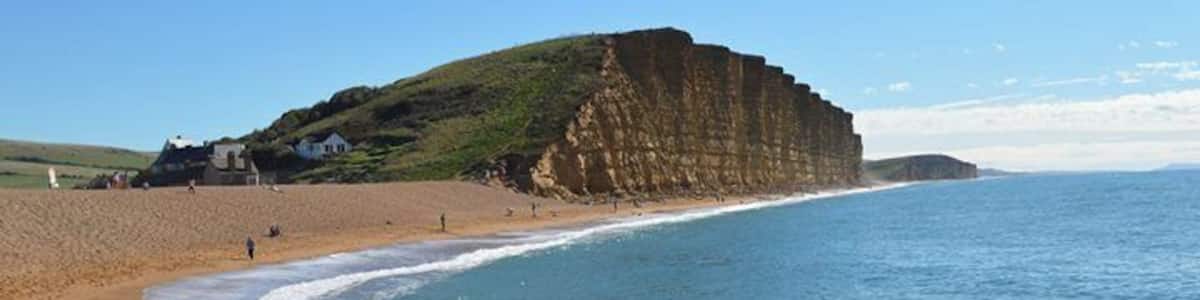 Ein Küstenstrand mit Klippen, klarem blauen Wasser und einigen Menschen, die am Ufer entlanggehen.