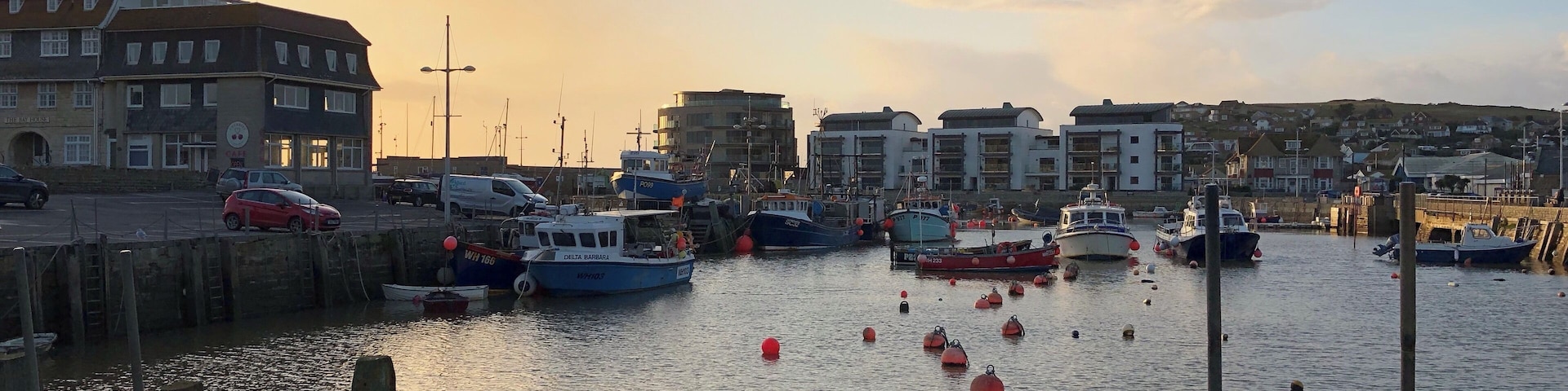 A harbor with boats, a red car, and buildings in the background.
