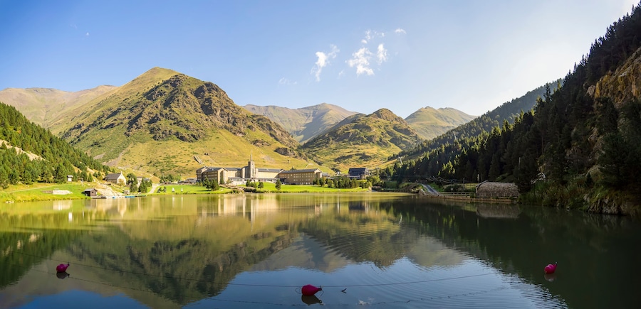 Un lago sereno con una iglesia y edificios en la orilla, rodeado de montañas y bosques frondosos.