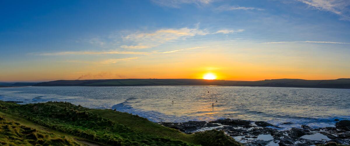 A sunset over a coastal landscape with rolling hills and a rocky shoreline.