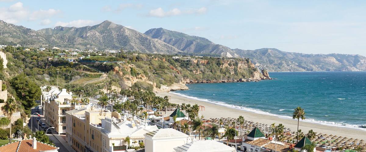 A coastal town with a beach, mountains, and buildings.