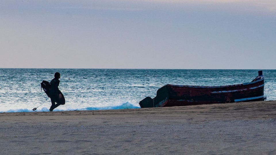 A person running along a beach with a boat in the water.
