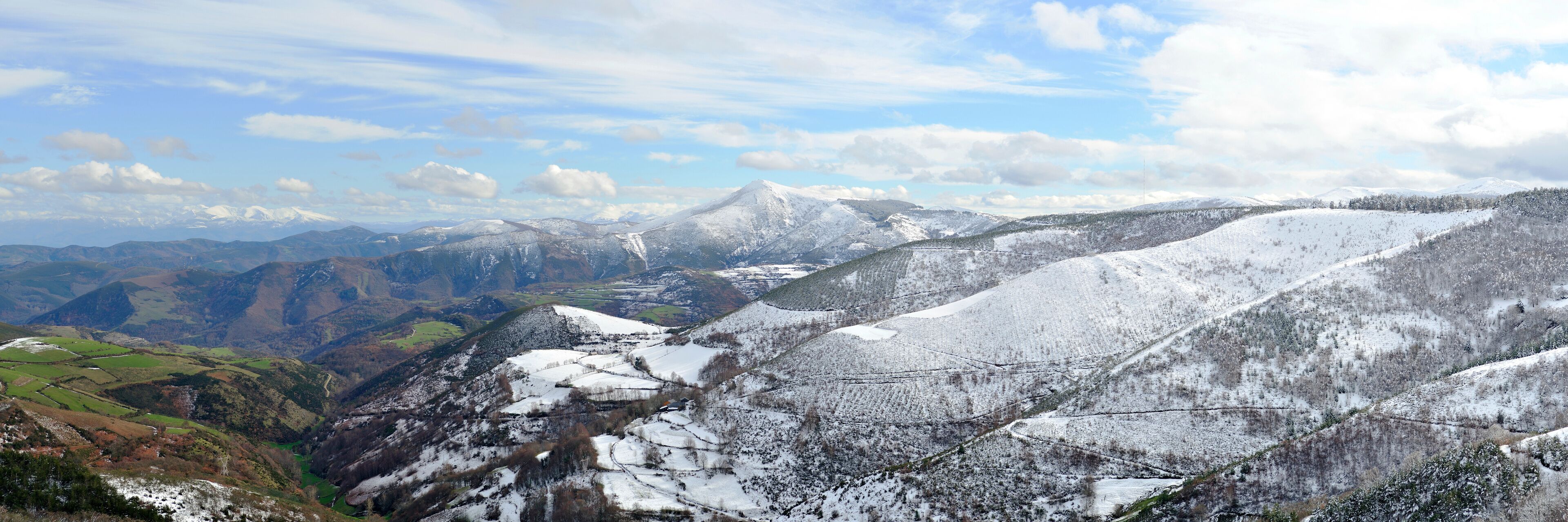 A snow-covered mountainous landscape with a valley and distant peaks.