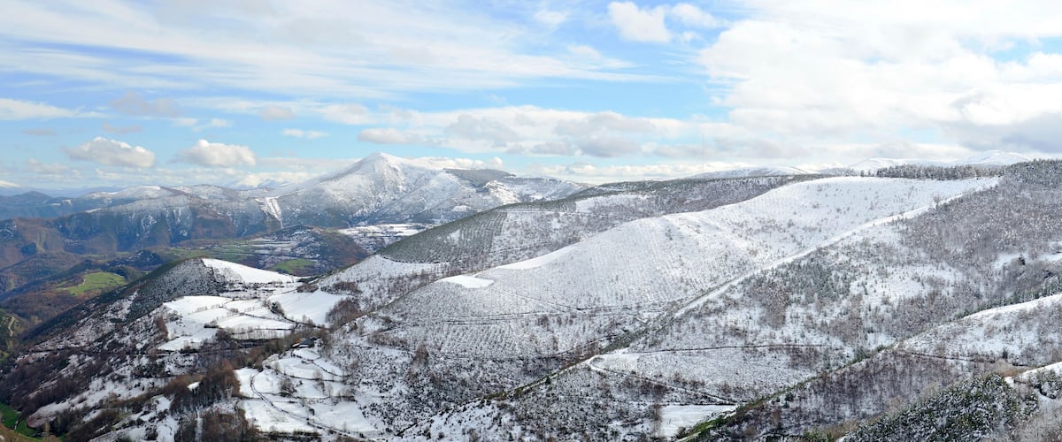 A snow-covered mountainous landscape with a valley and distant peaks.