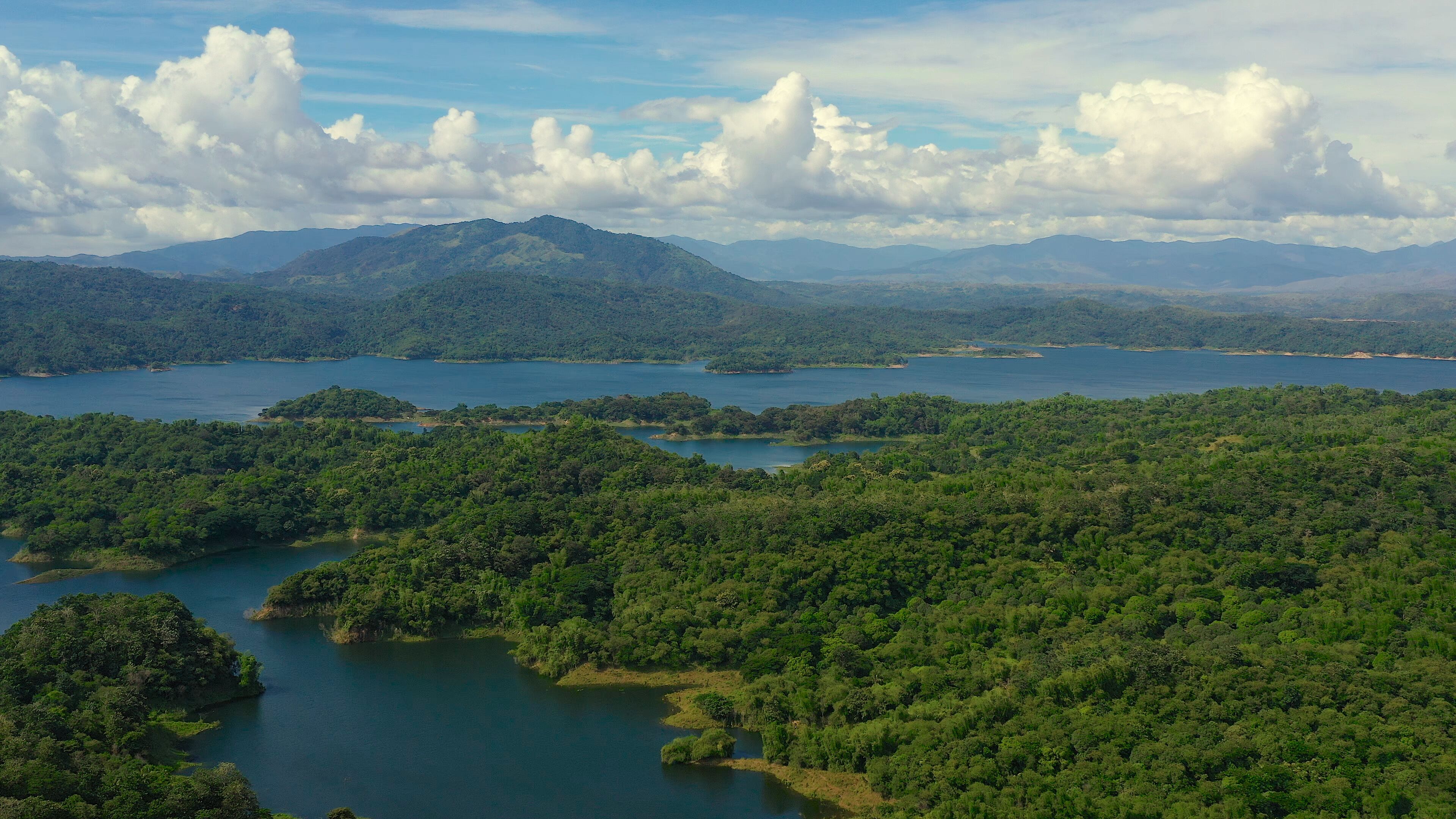 Clouds over a blue lake among green hills and mountains covered with rainforest. Aerial view: Pantabangan Lake. Philippines, Luzon.