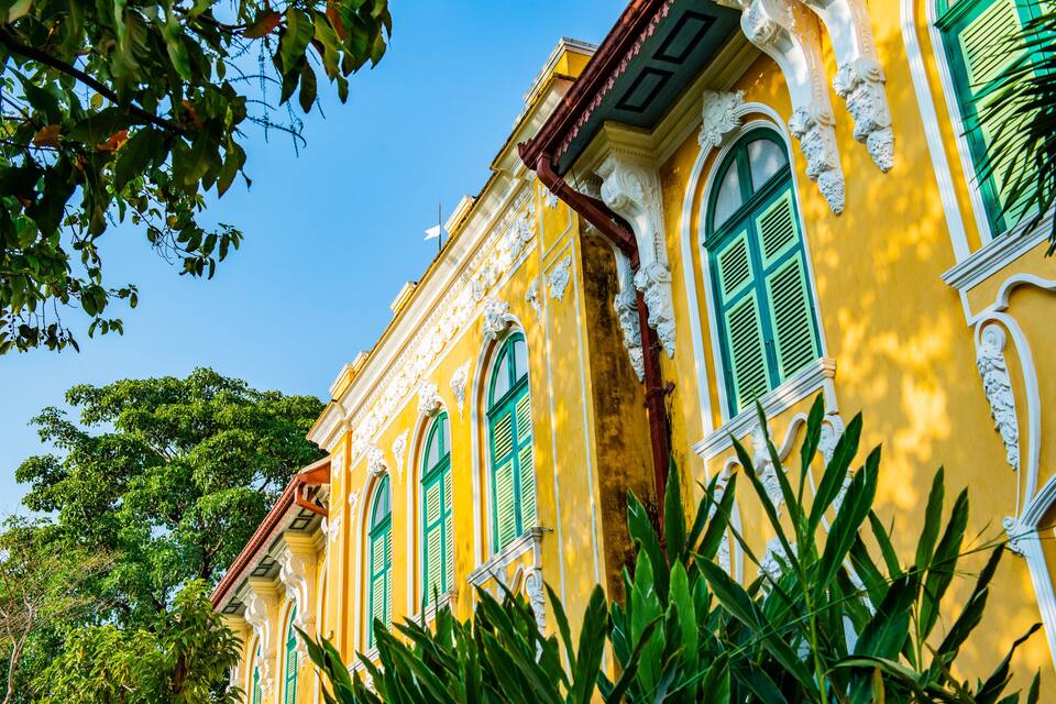 Un edificio amarillo con contraventanas verdes y adornos blancos ornamentales.