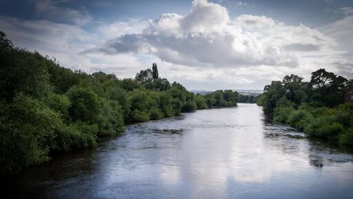 A river flanked by dense greenery and a partly cloudy sky.