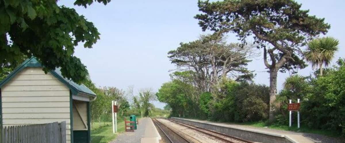 A railway station with tracks, a small shelter, and a signboard.