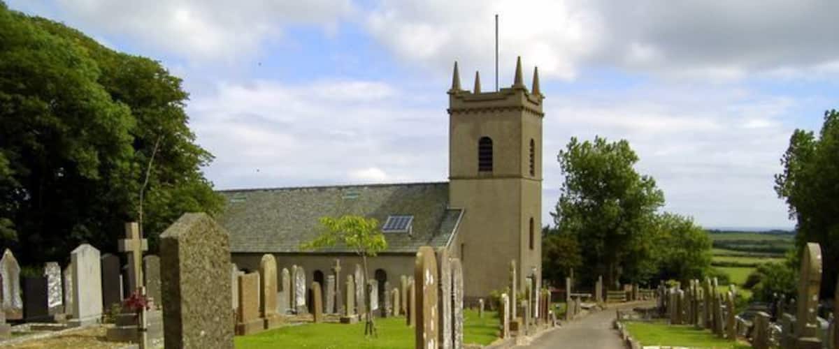 A churchyard with a prominent tower, rows of headstones, and a clear sky.