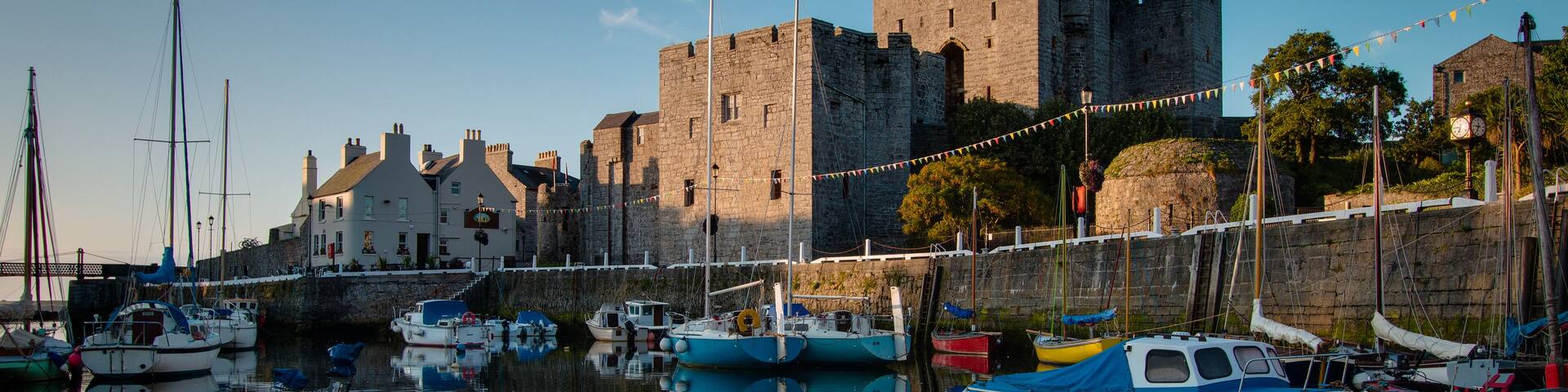 A historic castle with a moat, boats docked in the water, and a clear sky.