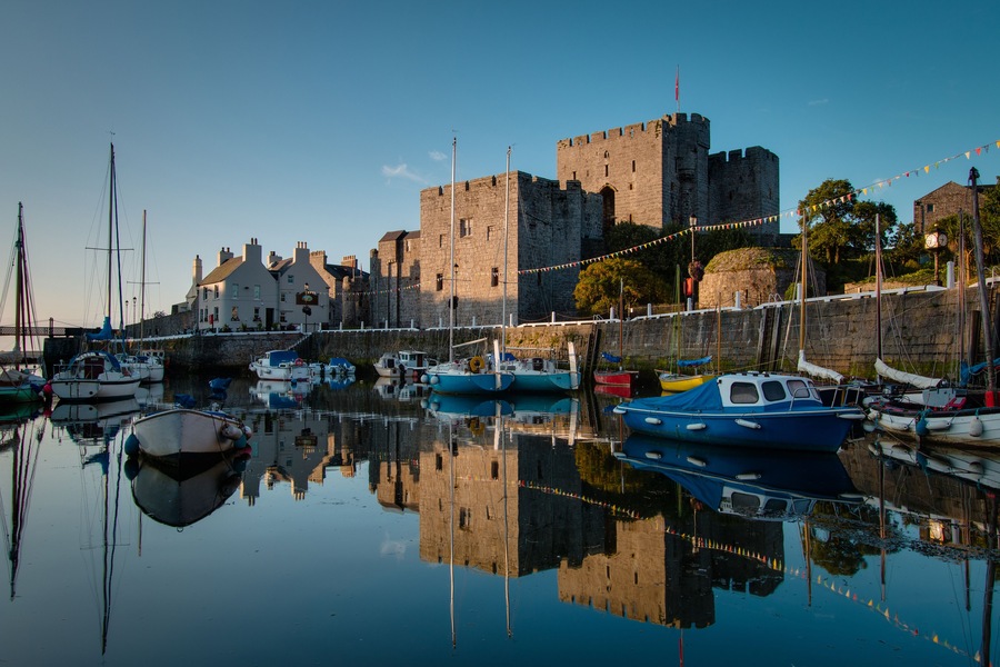 Sunrise at Castletown Harbor in the Isle of Man with Castle Rushen and boats reflecting in the water.