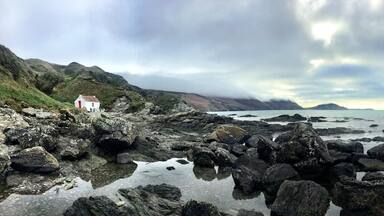 A rocky coastline with a white building on a hillside.