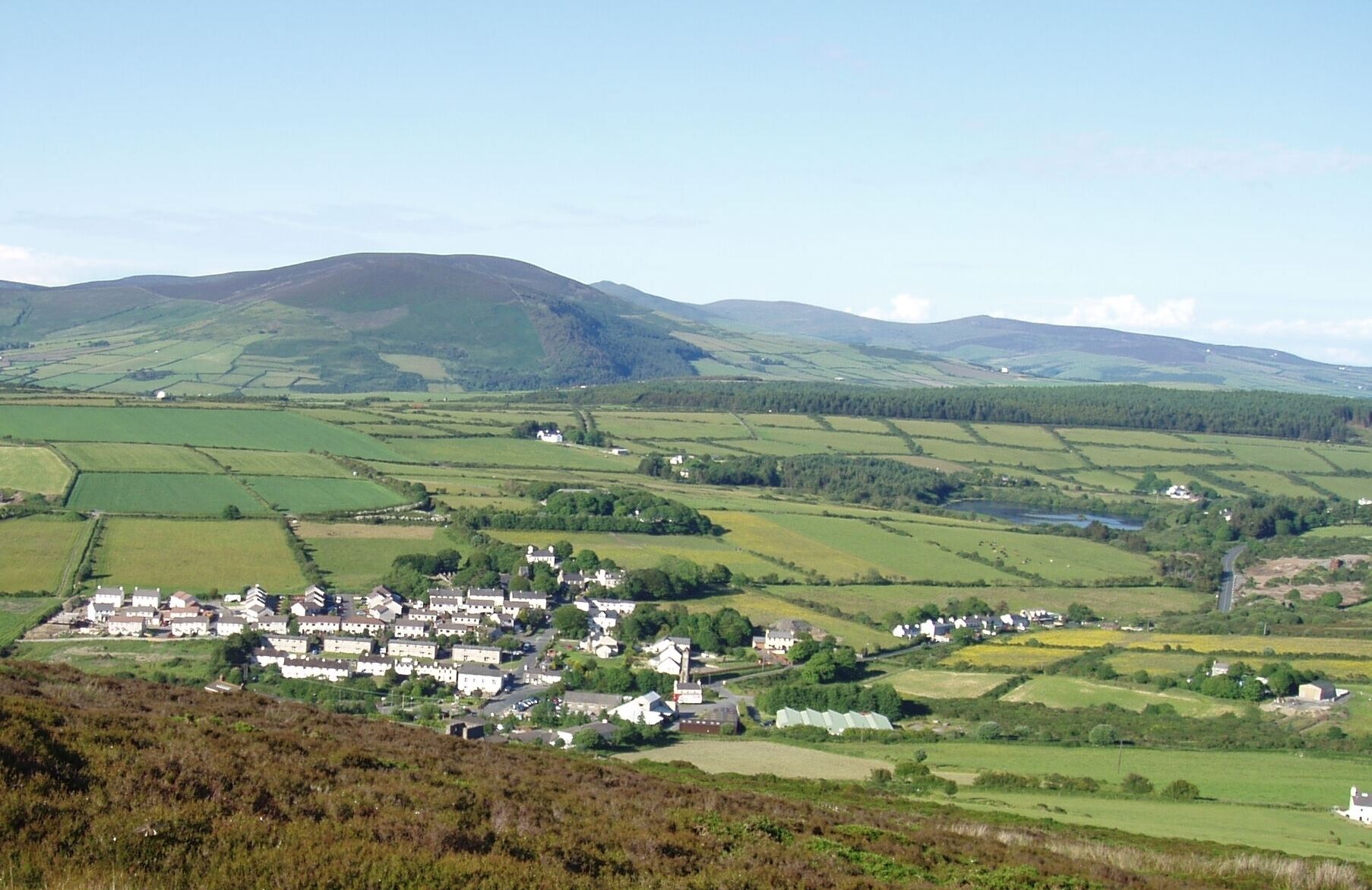 A rural village nestled in rolling hills with fields and scattered houses.