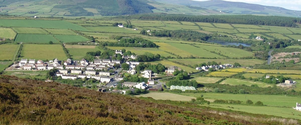 A rural village nestled in rolling hills with fields and scattered houses.