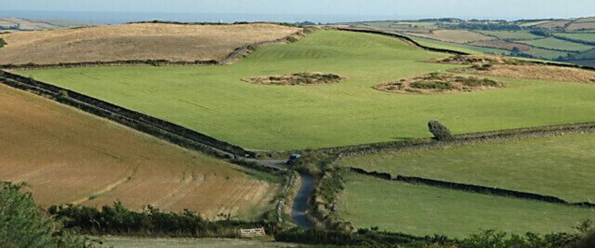 Rolling green fields, a narrow road, and distant hills.