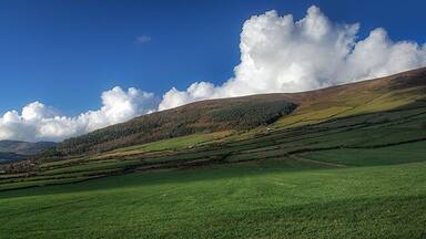 A green field, rolling hills, and a large cloud in a blue sky.